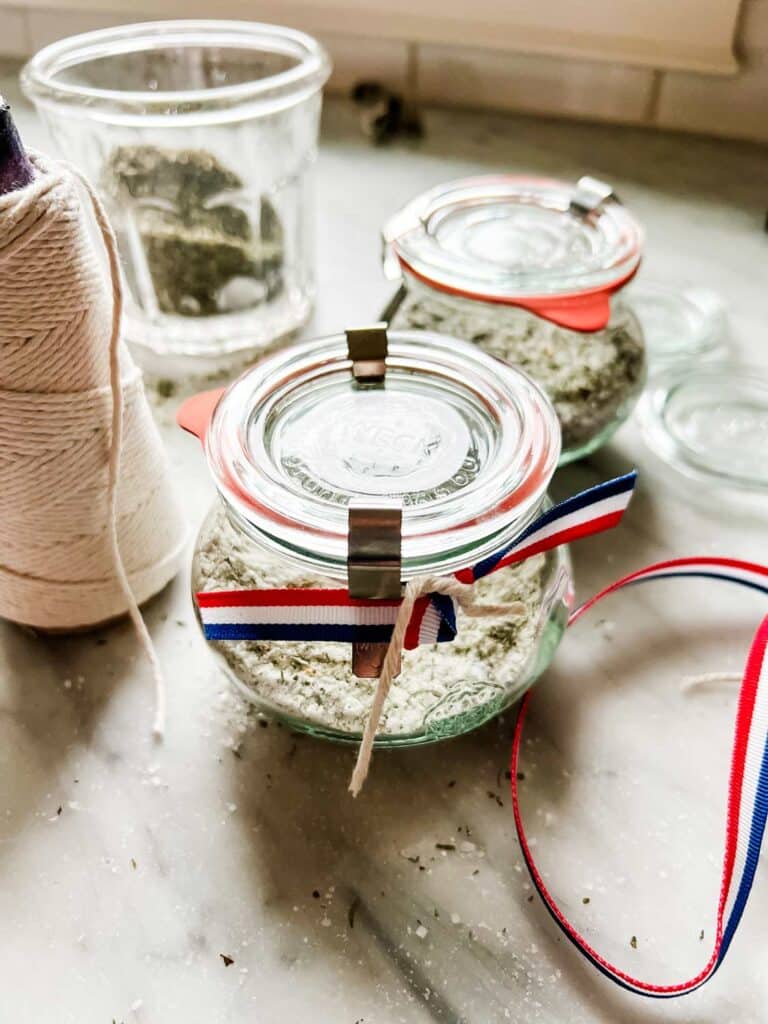 A jar filled with salt and French herbs is wrapped with a red, white, and blue ribbon to give as a parting gift from a dinner party.