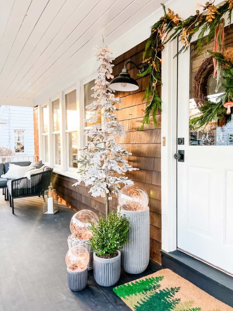 Garland, a white Christmas tree, and magical globe lights decorate the front porch for the holiday season.