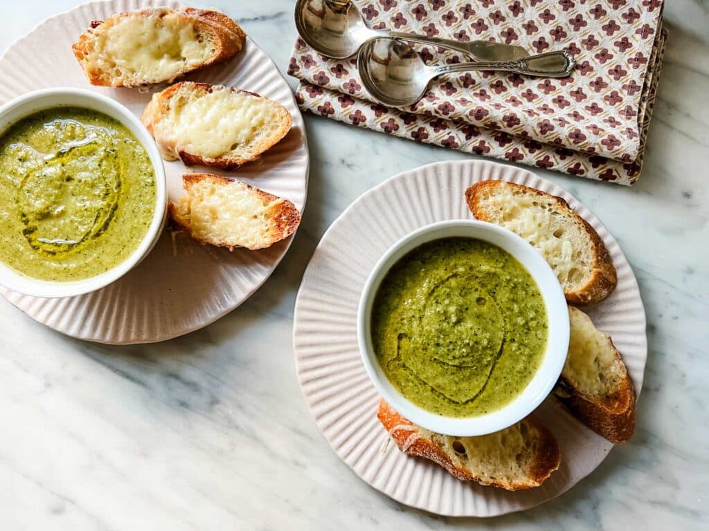 Two bowls of healthy broccoli soup are served with bagutte slices toasted with gruyere cheese.