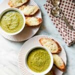 Quick and easy broccoli soup served in white bowls with toasted sliced baguette topped with cheese.