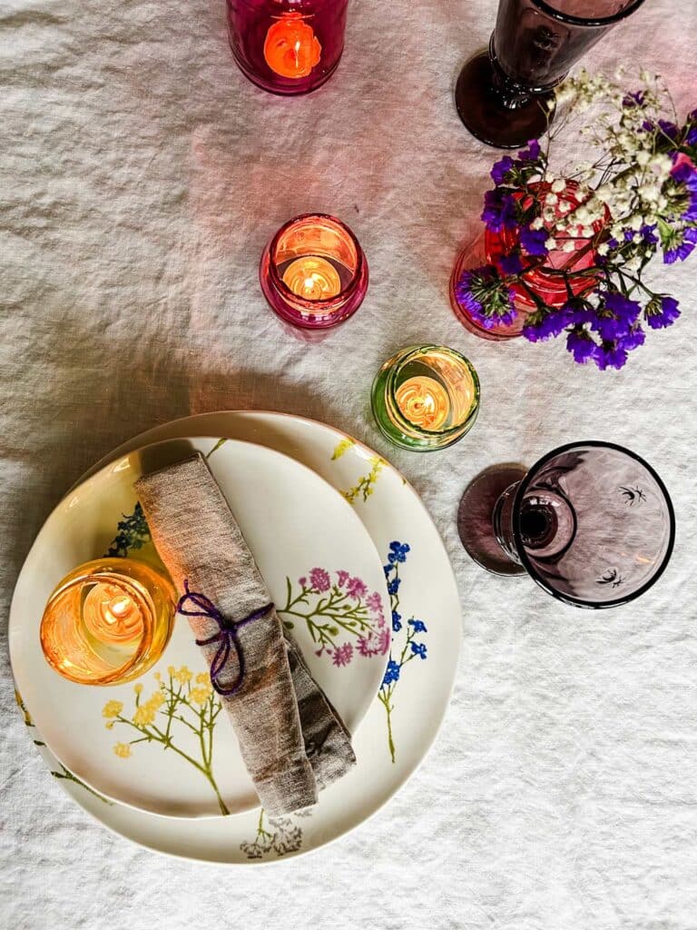 Floral plates are decorated with napkins tied with colored string and tinted colored jars for votives.