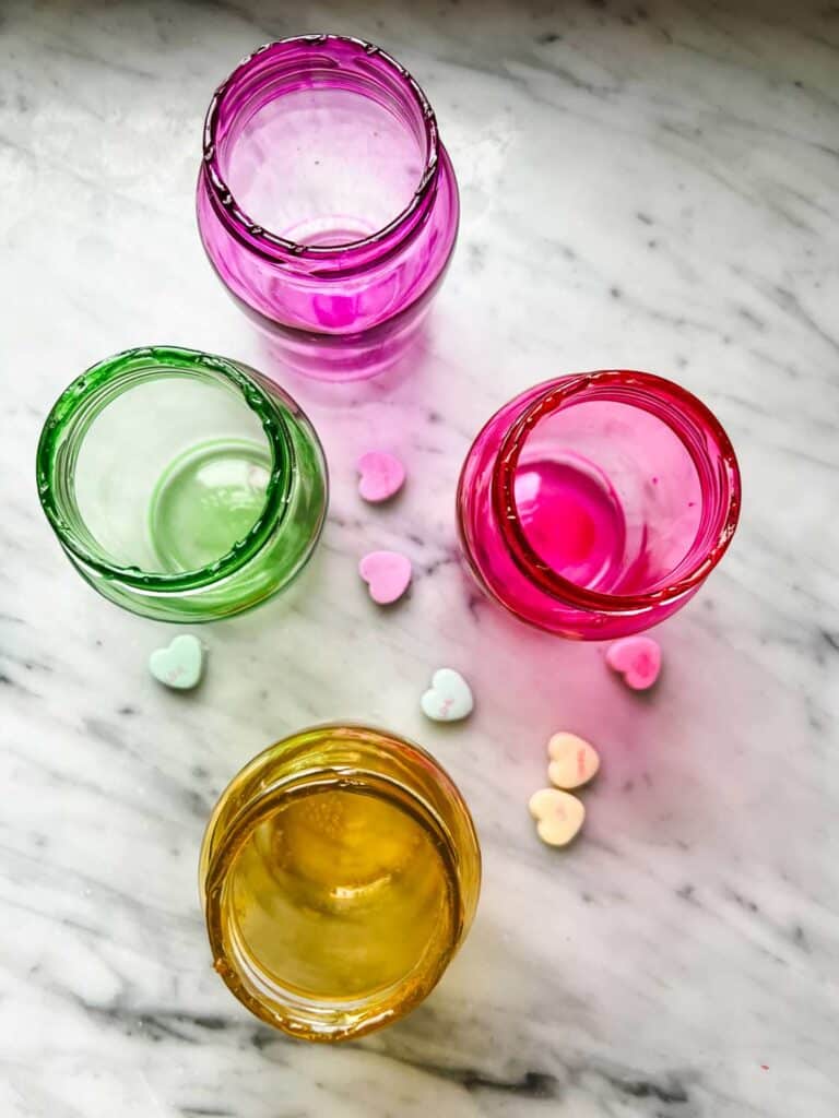 Green, purple, pink, and yellow glass jars with Valentine's conversation hearts in matching colors.