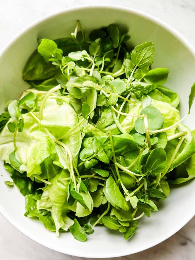 Mixed greens in a large white serving bowl.