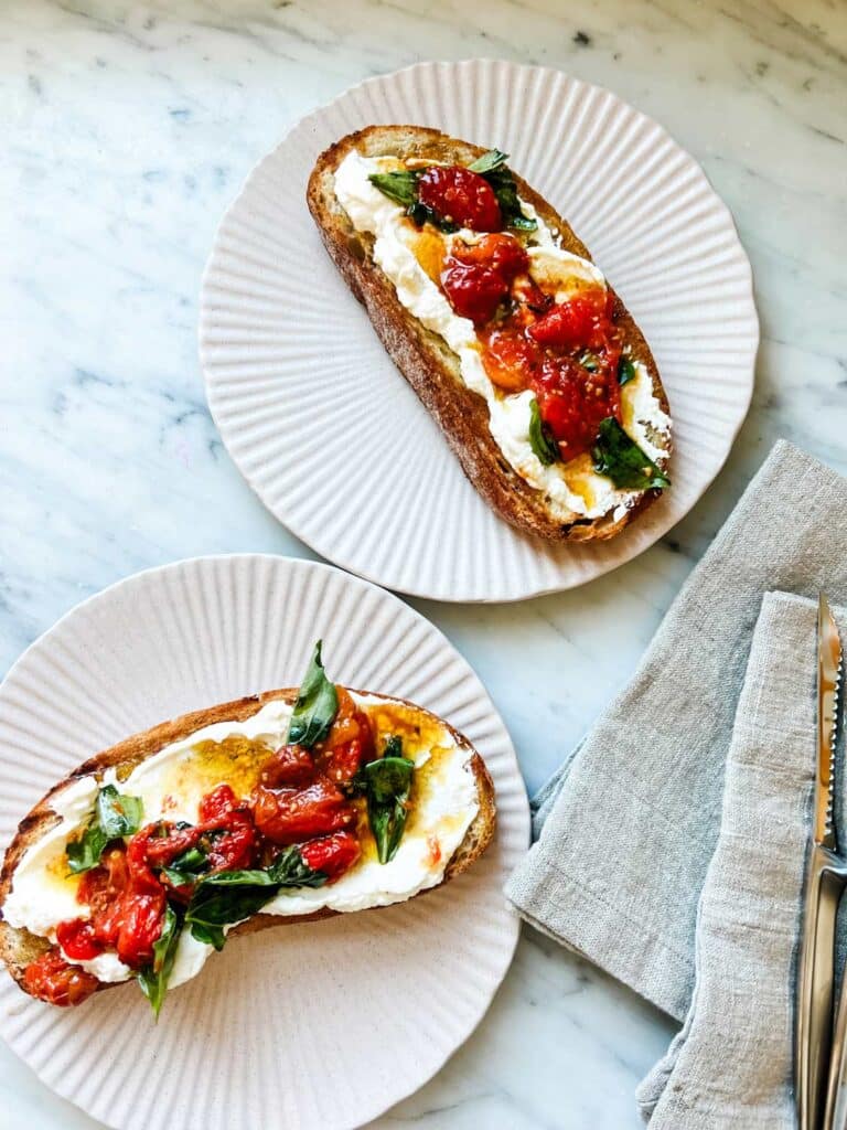 Garlicky ricotta and tomato confit tartines are served on small pink plates.