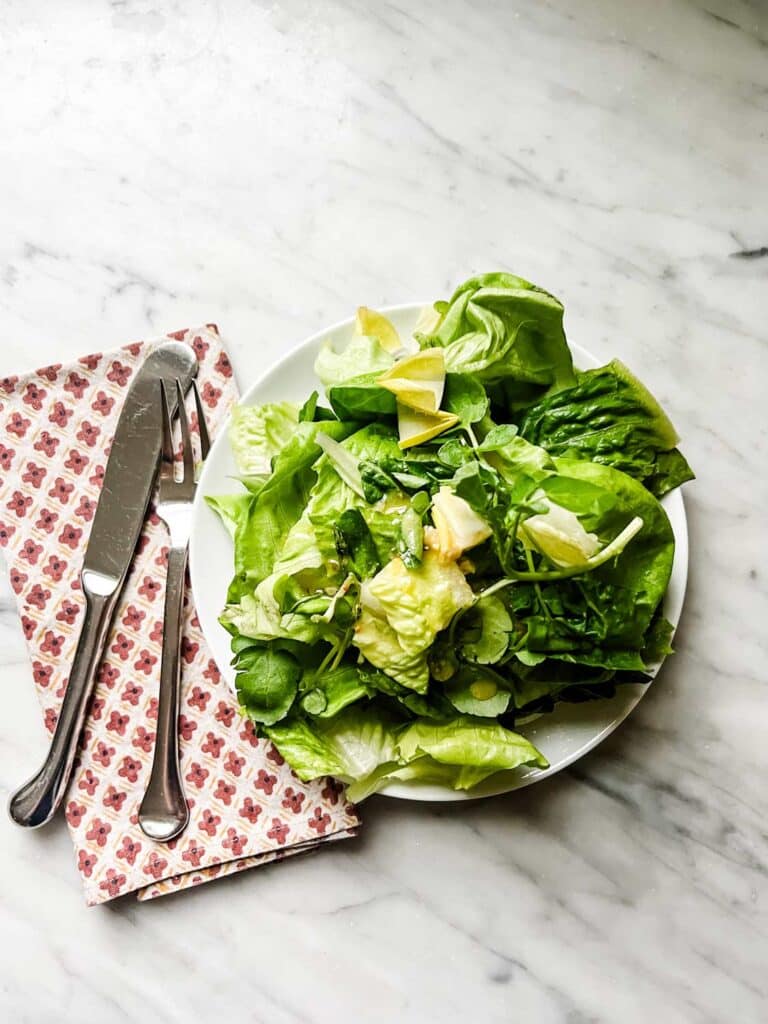 Via Cartoa's insalata verde is served on a small white plate with a fork, knife and napkin.