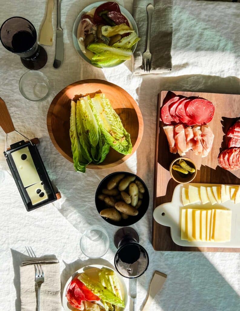 A table is set, cheese is melting on a mini-Raclette machine and wine has been poured. 