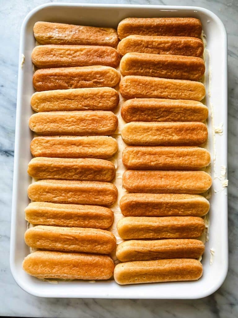 Ladyfinger cookies soaked in lemon syrup lay flat in a baking dish.