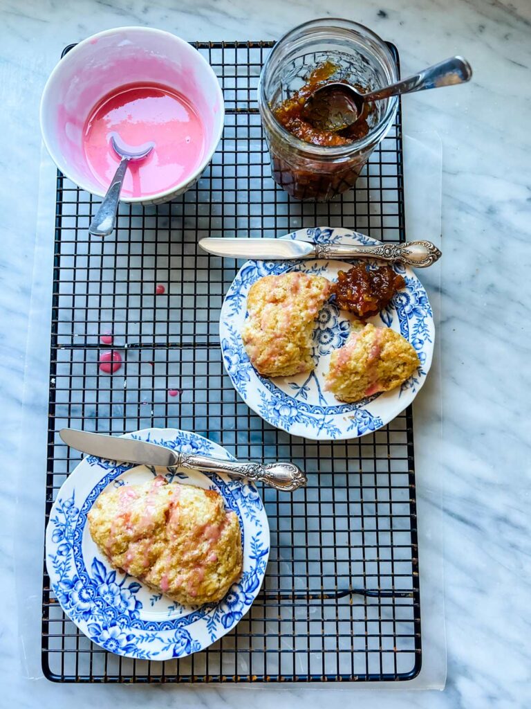 scones on plate, knife, small bowl with pink glaze, spoon, jar of marmalade 