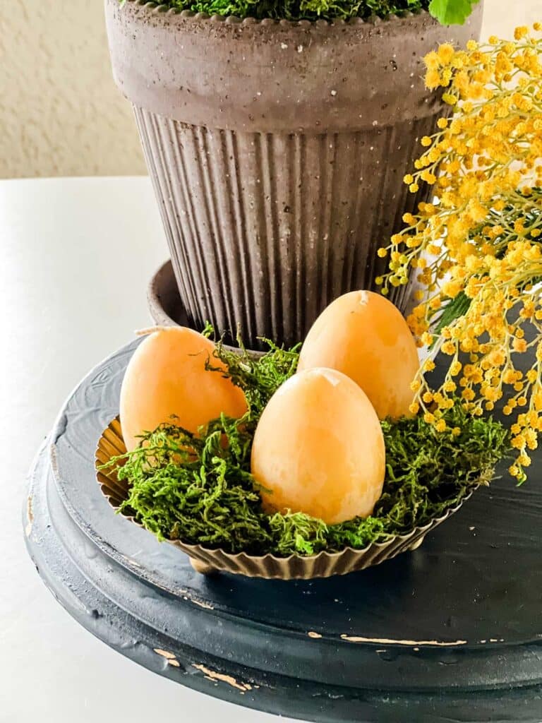 Egg-shaped candles with a potted plant and fresh mimosa flowers.