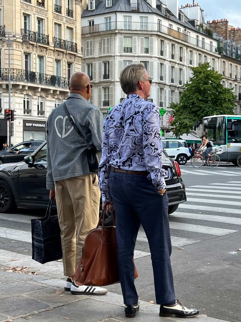 Two men on the streets of Paris waiting to cross the street. One is wearing Adidas Samba sneakers.