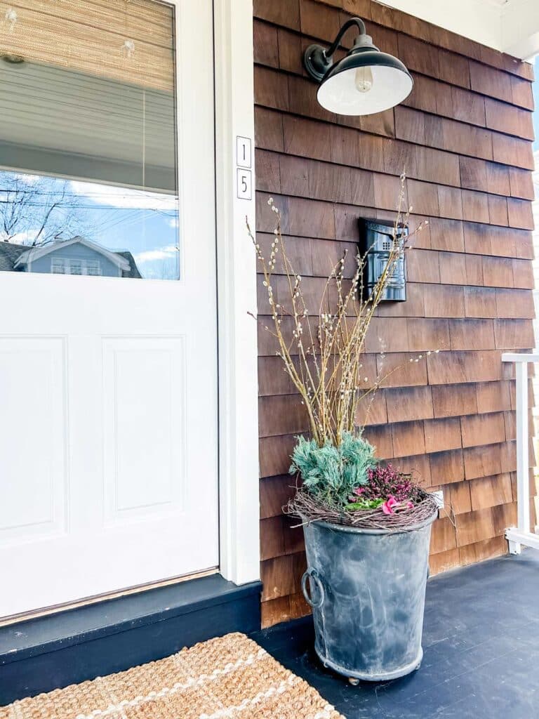 A porch planter with spring flowers sit next to the front door of this cottage-style house. Liners and a plugged drain hole keep the water from leaking onto the porch.