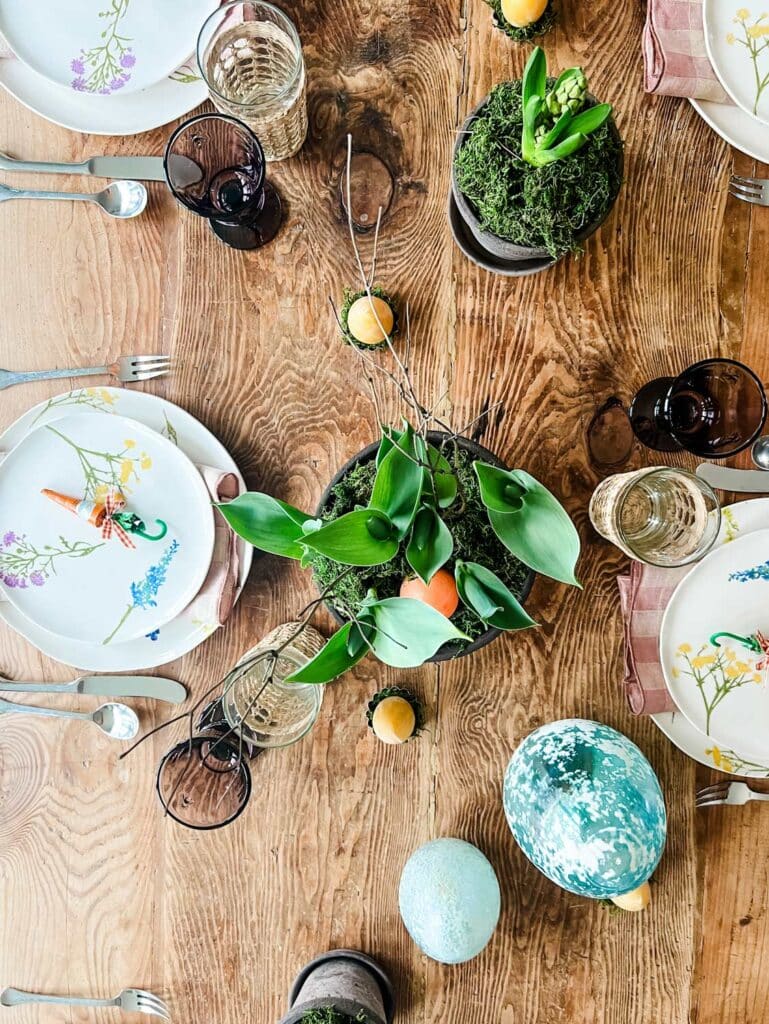 Colorful Easter table with floral plates, plaid napkins, glassware and Bergs pots filled with spring plants and moss 