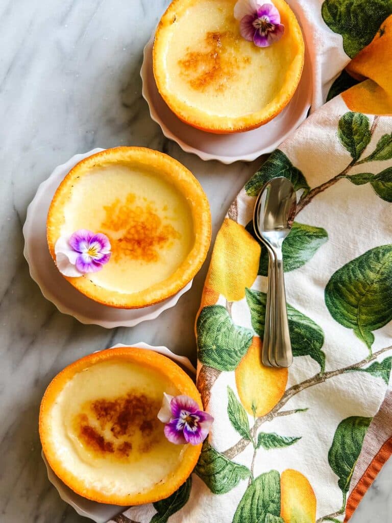 Creamy orange posset is served in orange peel cups on small white saucers.