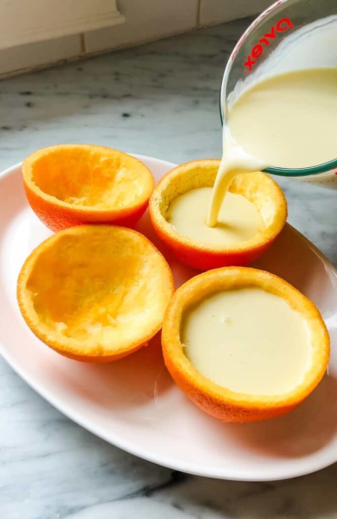 Hollowed-out orange peel cups are being filled with orange posset.