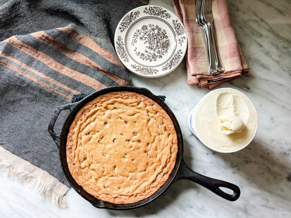 A giant skillet chocolate chip cookie baked and fresh from the oven. Vanilla ice cream is ready to go on top.