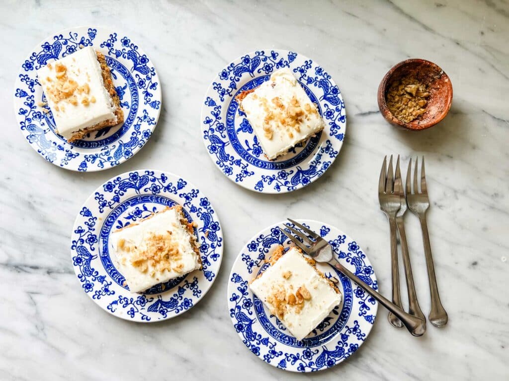 Squares of low-carb carrot cake are cute blue and white French plates. Each square of the cake has chopped nuts sprinkled on top.