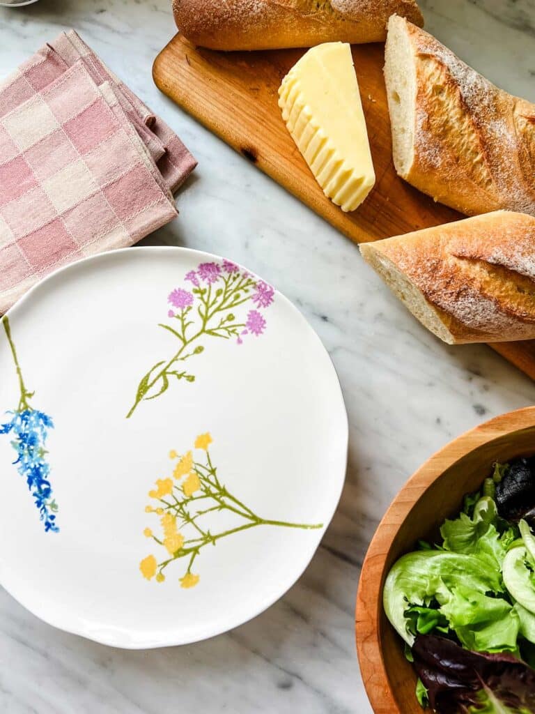 Plates and napkins next to a baguette, French butter and a side salad.