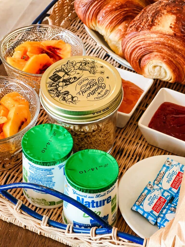 A breakfast tray features fresh peaches, yogurt, granola, butter, preserves and croissants.
