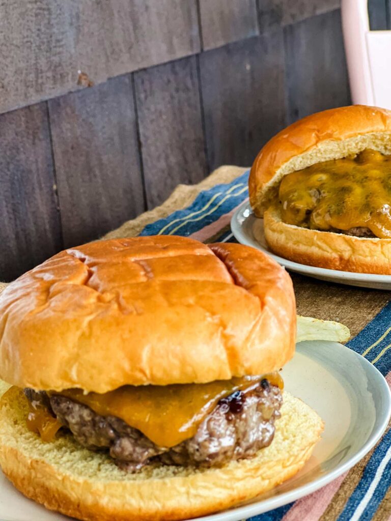 Two grilled cheeseburgers served on a small outside table.