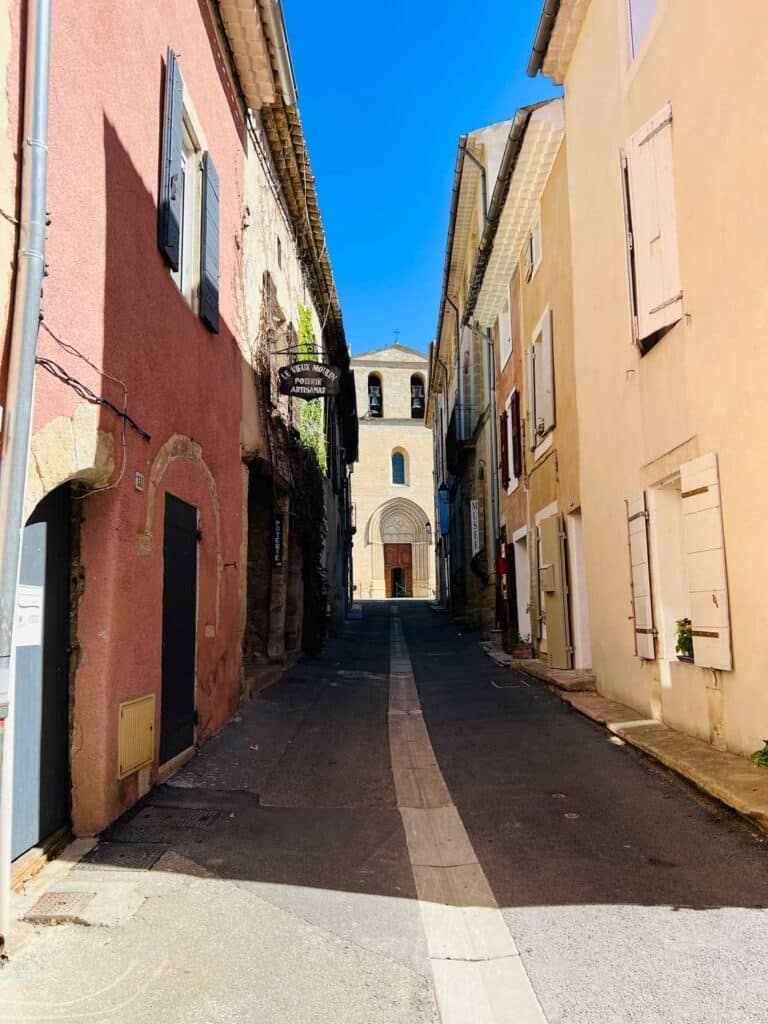 An old stone path, covered in shadows, with brilliant blue sky in the background, leads to the shops and homes of Cucuron, France.