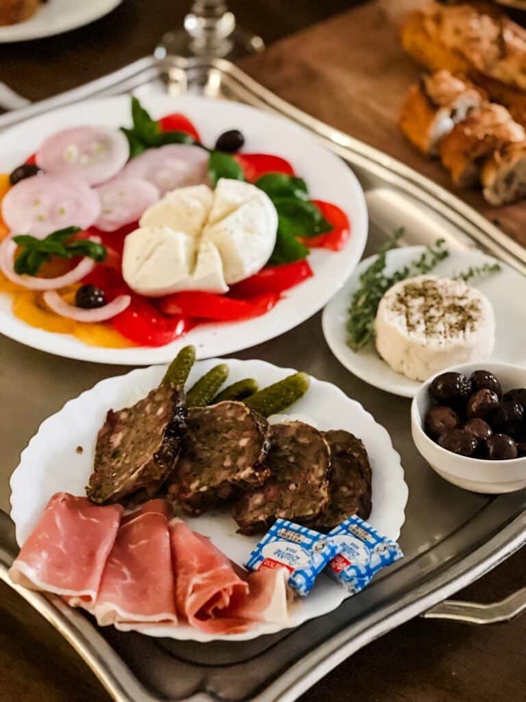 A tray for a late night dinner snack features red and yellow tomatoes, sweet red onions, a variety of meats and cheeses and bowl of olives.