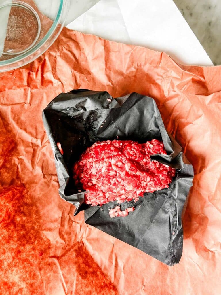 A pound of fresh ground beef is triple-wrapped in white, brown, and black paper.