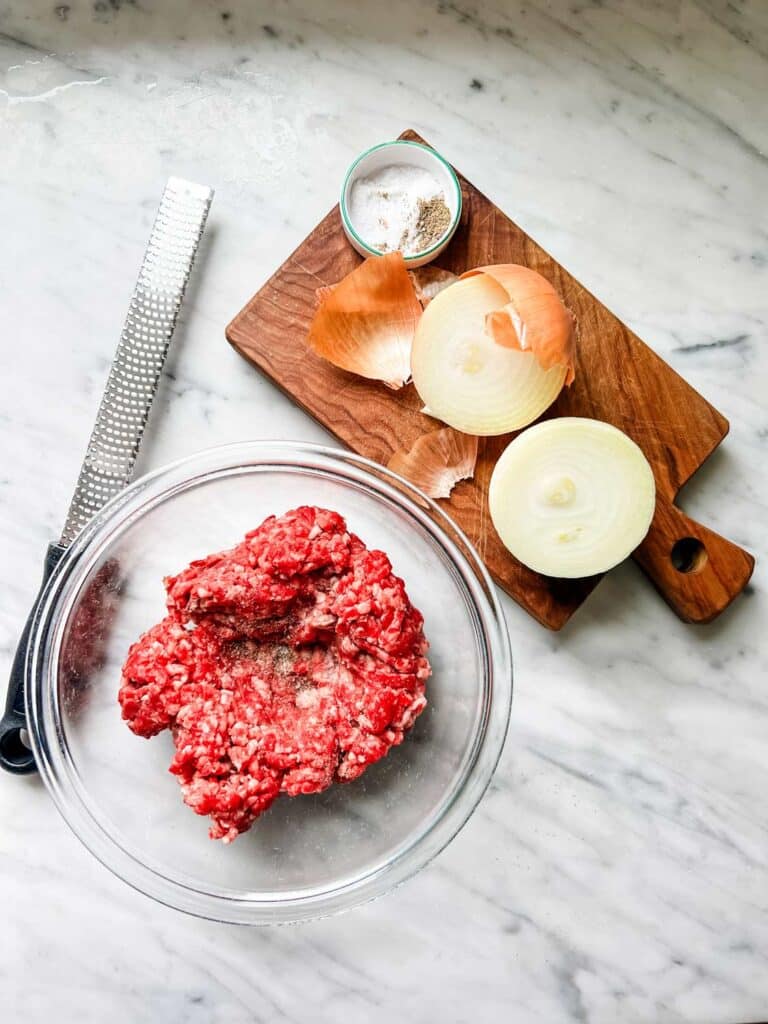 Ground beef in a bowl is ready for grated onion and salt and pepper. These are part of the secret ingredients for making the best grilled burgers.