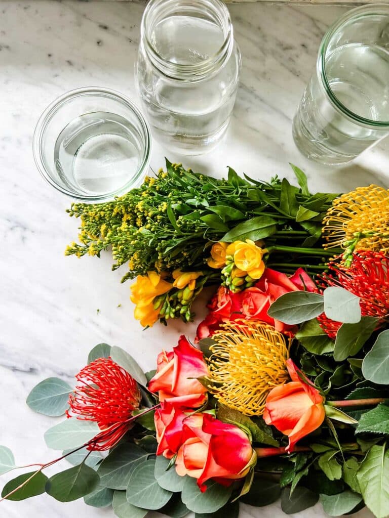 Orange and yellow flowers with greenery are on the kitchen counter next to tall glass jars.