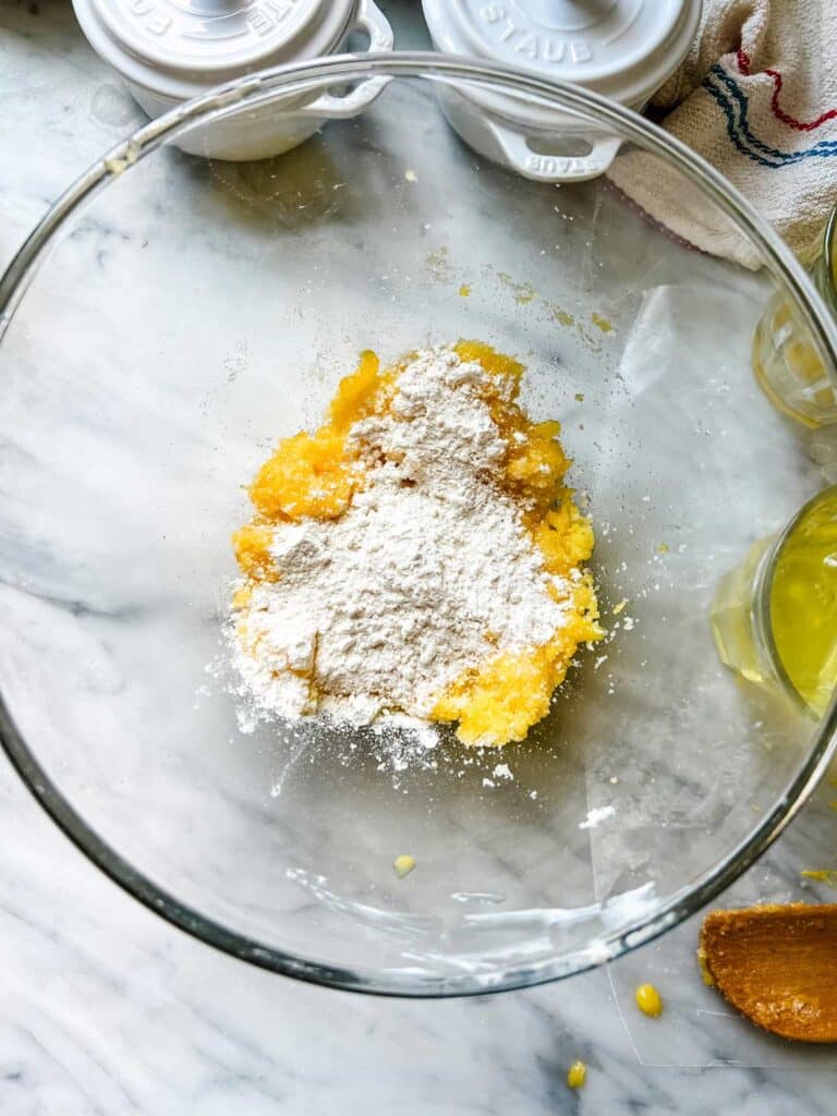 Flour is added to the sugar, butter, and egg yolk mixture for a baked lemon pudding recipe.