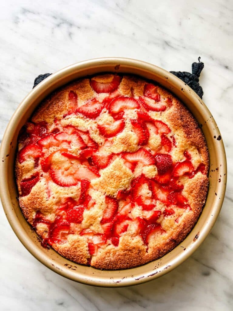 A summer strawberry spoon cake has been baked to a golden brown and is resting on the kitchen counter to cool before serving.