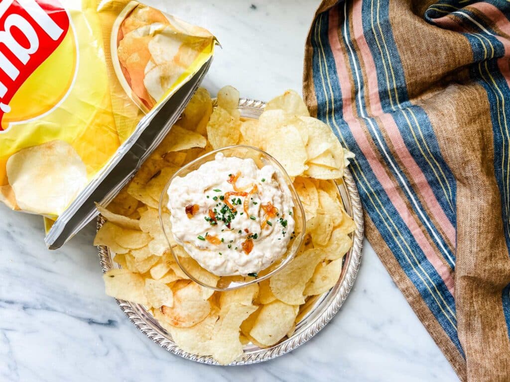 Old fashioned caramelized onion dip served in a small bowl with a platter of Lay's potato chips.