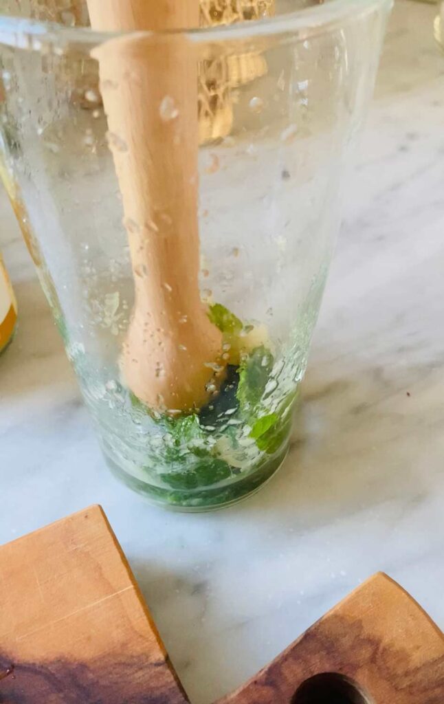 A wooden muddler is mixing ingredients for a mojito mocktail.