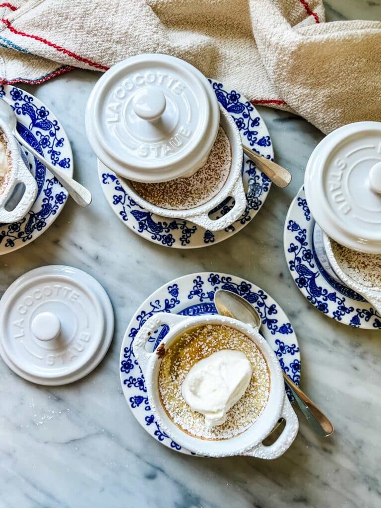 Baked lemon pudding in mini Staub cocottes is served on small blue plates with spoons.