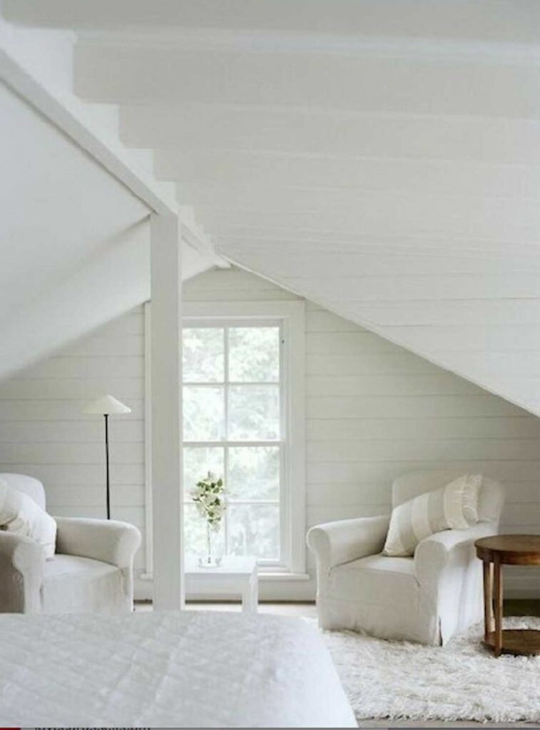 Two white denim slip-covered chairs are next to a large window. The walls, floors, ceiling and bedspread are also white.