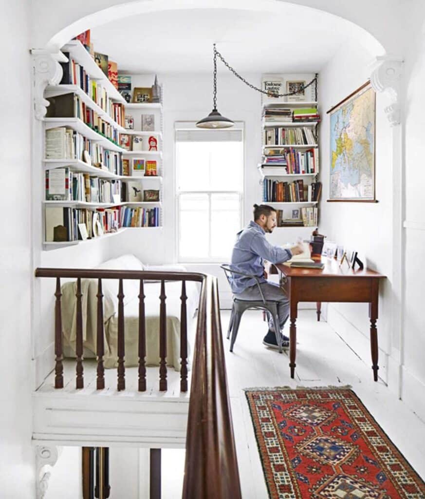 A landing area serves as a small workspace. The walls and floors are painted white and the walls are lined with bookshelves.