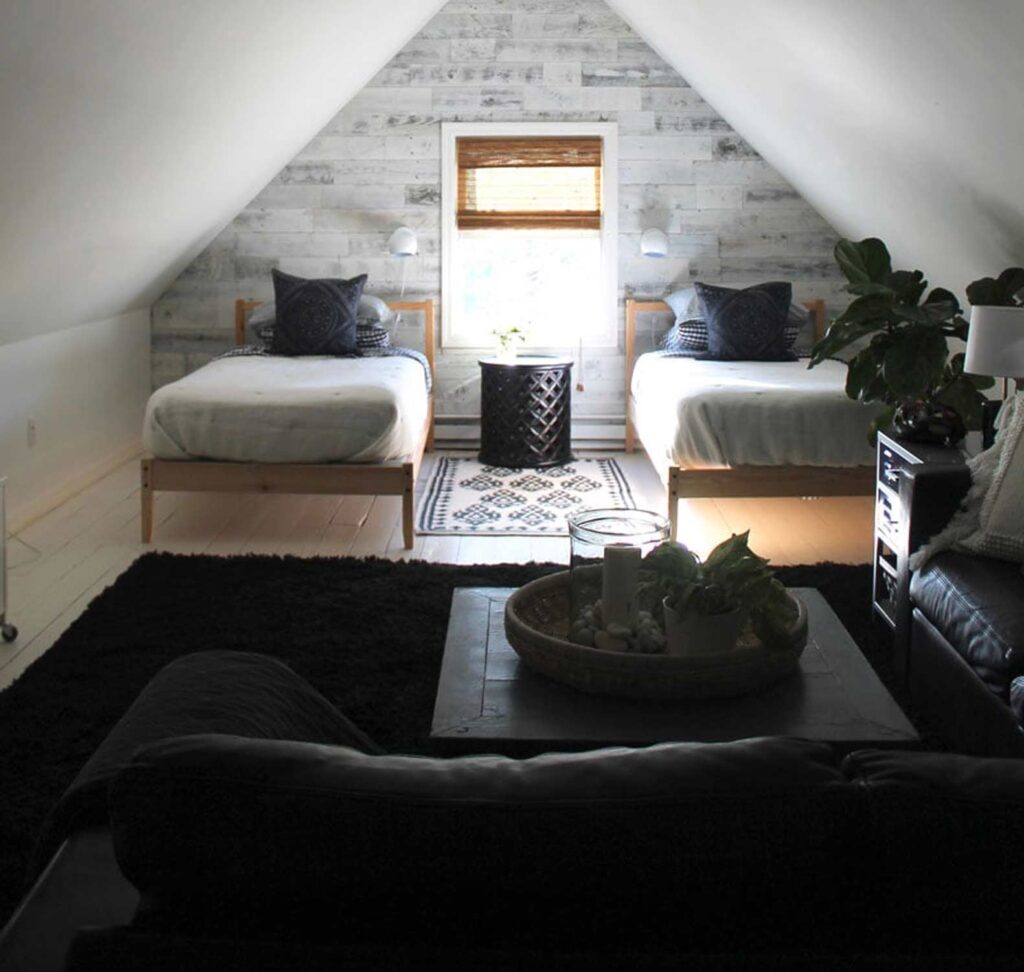 A black leather couch and black shag carpet in the foreground of an attic hangout and guest space. Twin beds are in the background.