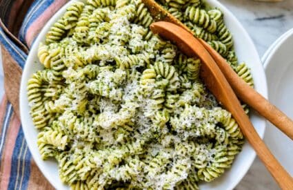 Basil pesto pasta sauce in a large white serving bowl and wooden spoons.