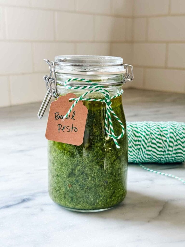 An airtight jar is filled with fresh basil pesto with a thin layer of olive oil on top to help keep its vibrant green color.