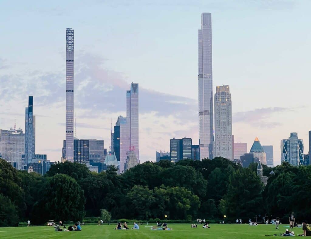People relaxing on one of the lawns in New York City's Central Park and the skyline is in the background.