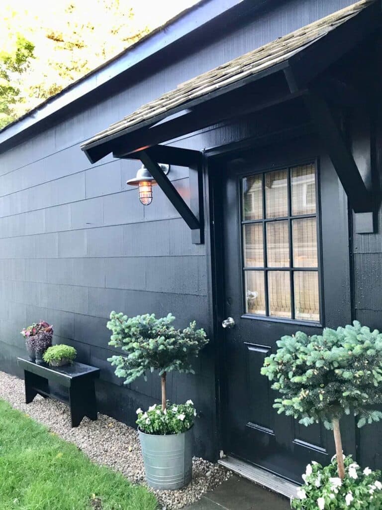 Potted plantings sit next to the side door of a garage with a portico.