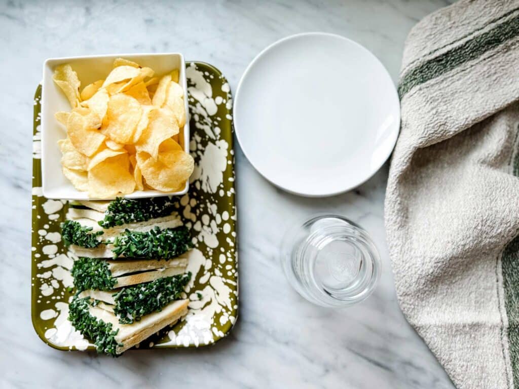 Cucumber sandwiches with Chive Sprinkles. White plates, glasses, green and white tray with potaot chips in white sqaure bowl.