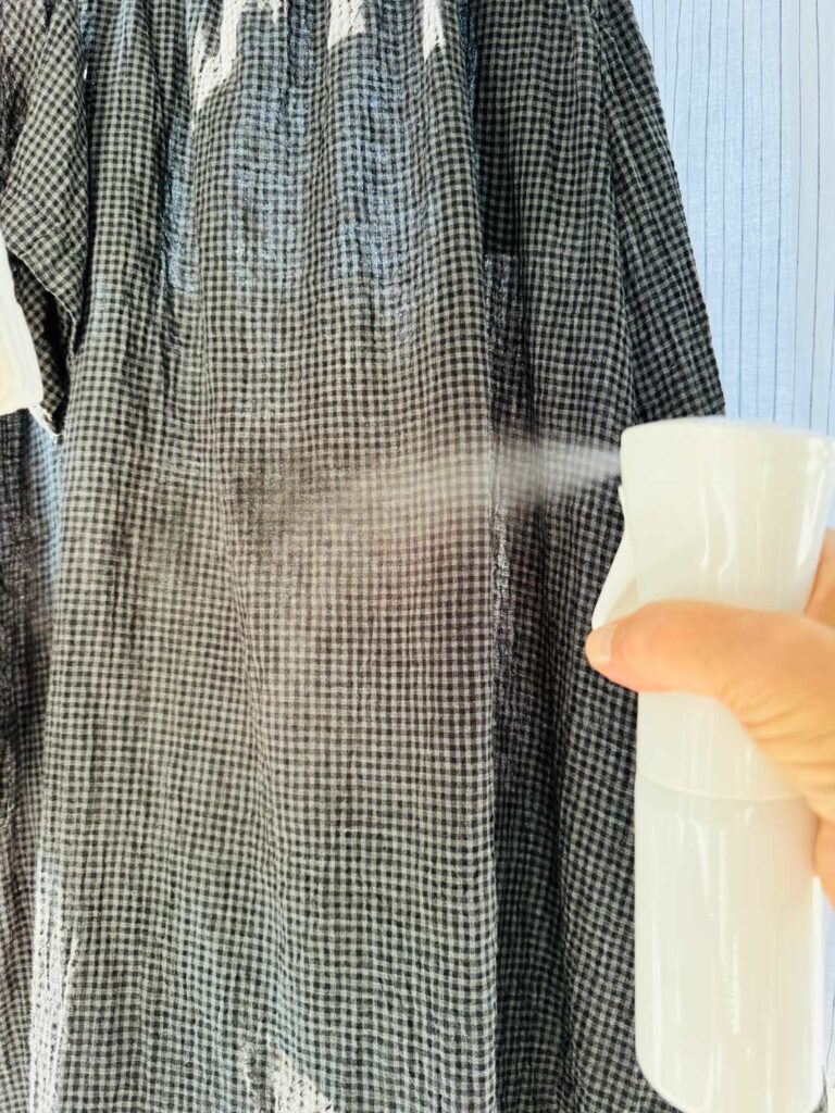 spraying a black gray chked skirt with a fine mist. Woman's hand holding spray bottle.