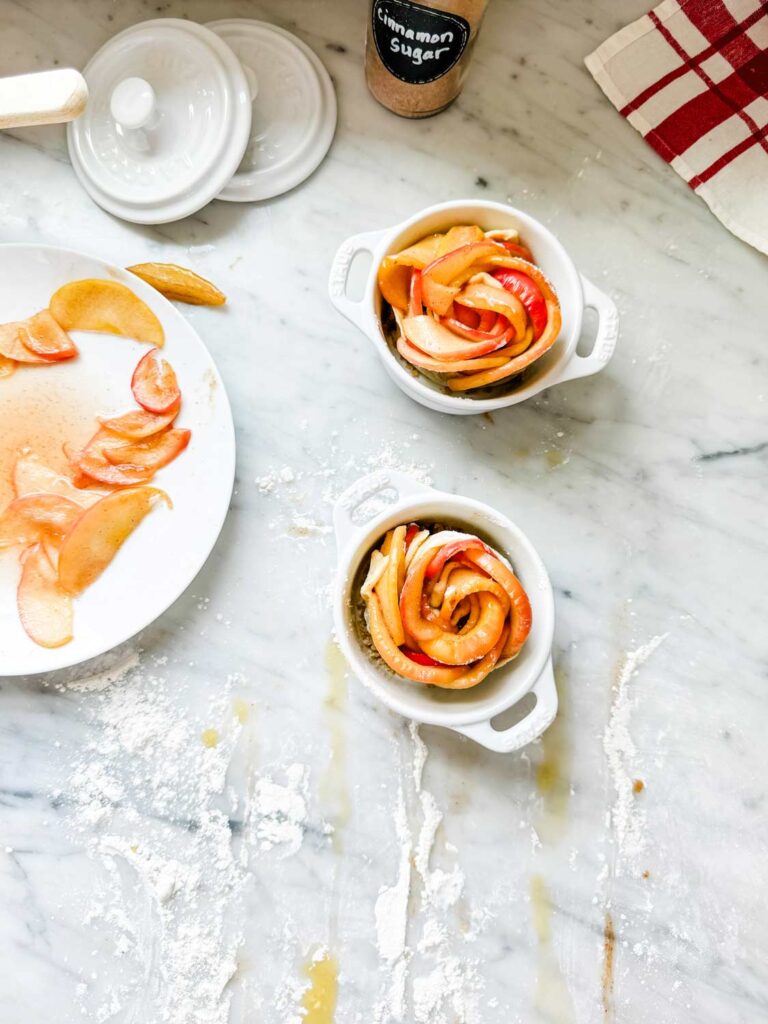 Puff pastry filled with cooked apples has been rolled up to form the shape of a rose and placed in min Staub cocottes.