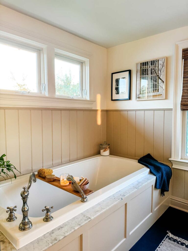 Large bath tub with shelf, dark gray towel, photos hanging at end of tub. Chrome fixtures. 