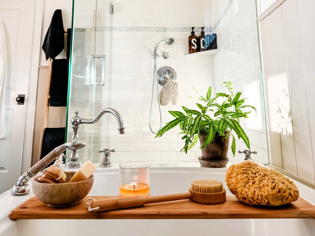 Primary bathroom refresh: small ideas to inspire you. Wood bath shelf on tub woth candle, soap, bowl, brush, sponge.