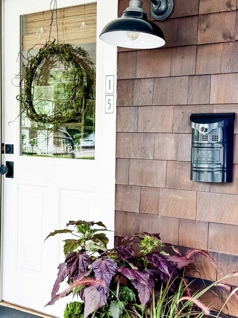 A Faux Mossy Twig Wreath for Halloween  on white door. Blsack metal mailbox to the right with house numbers 15 on the door frame. 