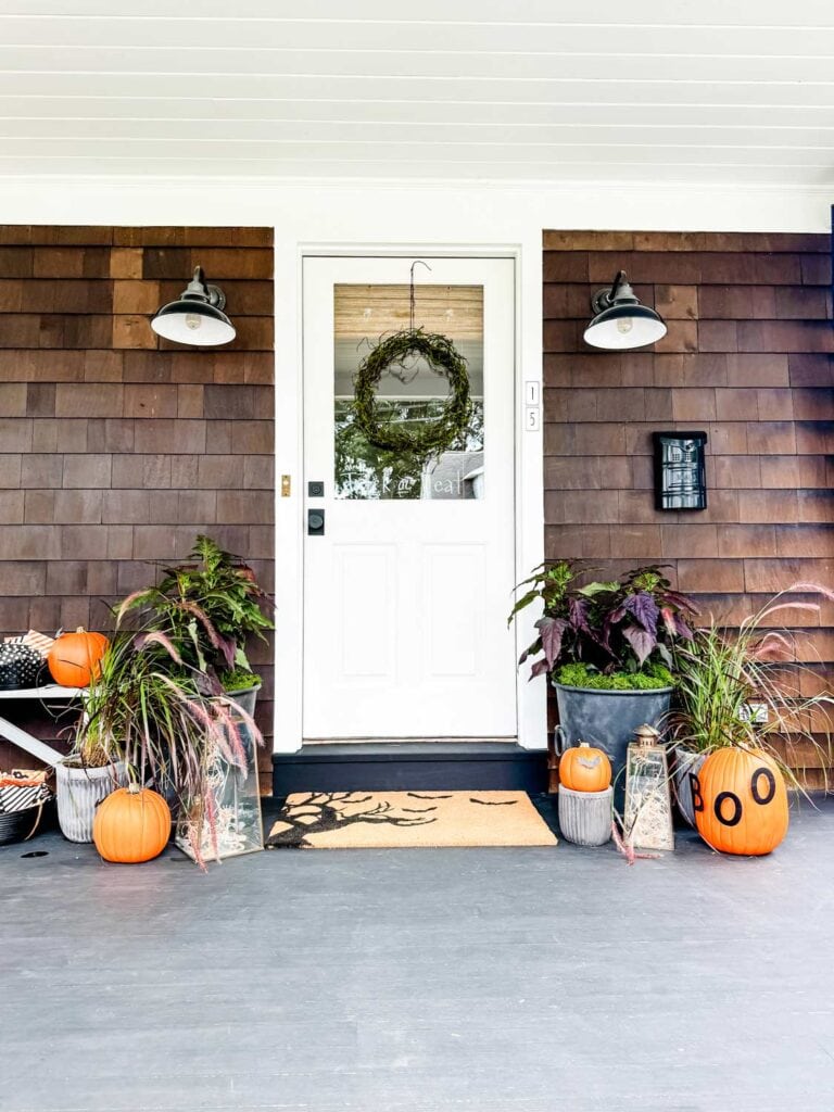 A Faux Mossy Twig Wreath for Halloween  on white door. Blsack metal mailbox to the right with house numbers 15 on the door frame, pumpkins, planters.