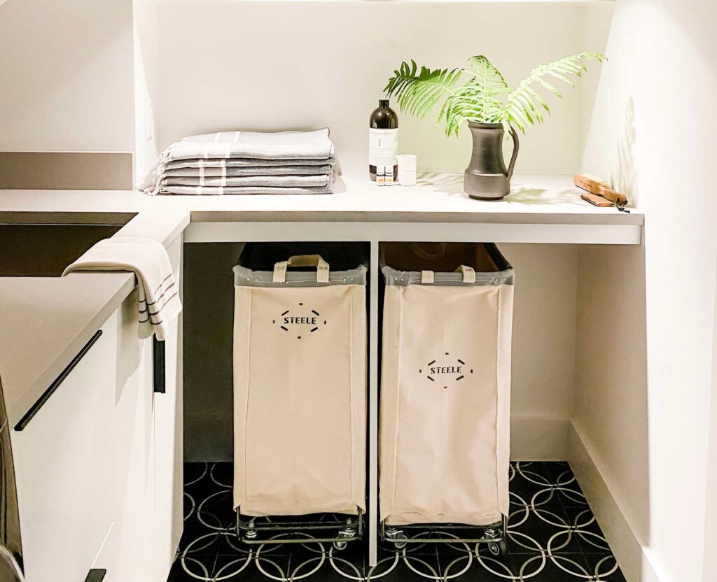 Rolling bins under the counter, fern in black pitcher, stacked gray towels. 