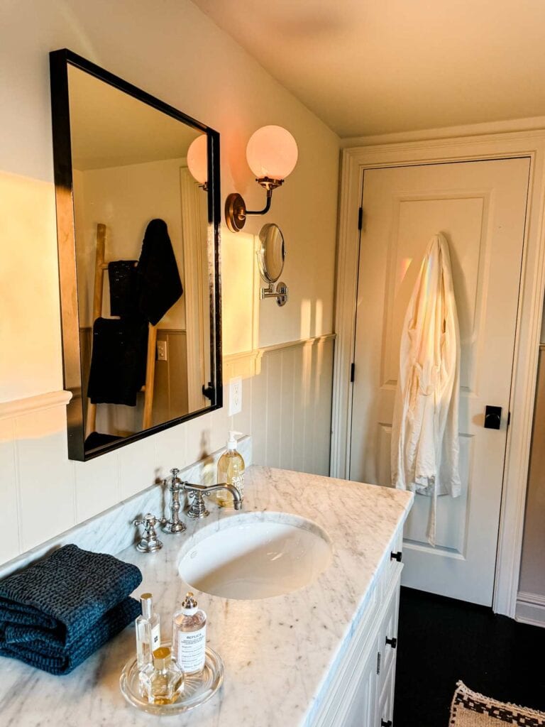 mirror, sconce, marble countertop, sink, soap bottle, fragrances on crystal tray.