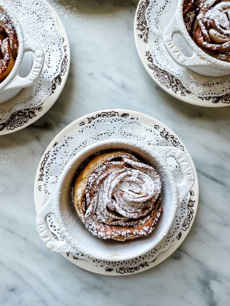 Puff pastries with apples resemble roses and are dusted with powdered sugar. They are in mini Staub cocottes. 